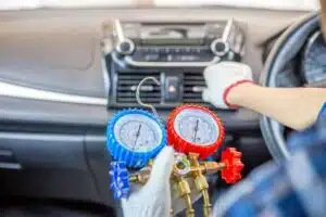 A technician performing car AC repair service, using a pressure gauge to check and recharge the air conditioning system.