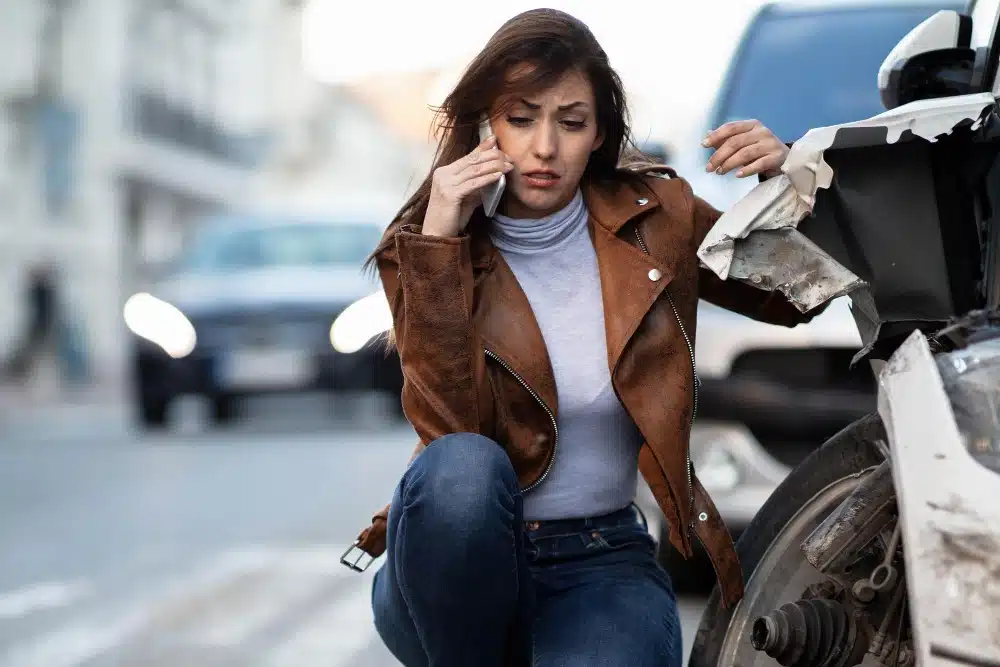 Woman kneeling beside a damaged car after a collision on a city street.