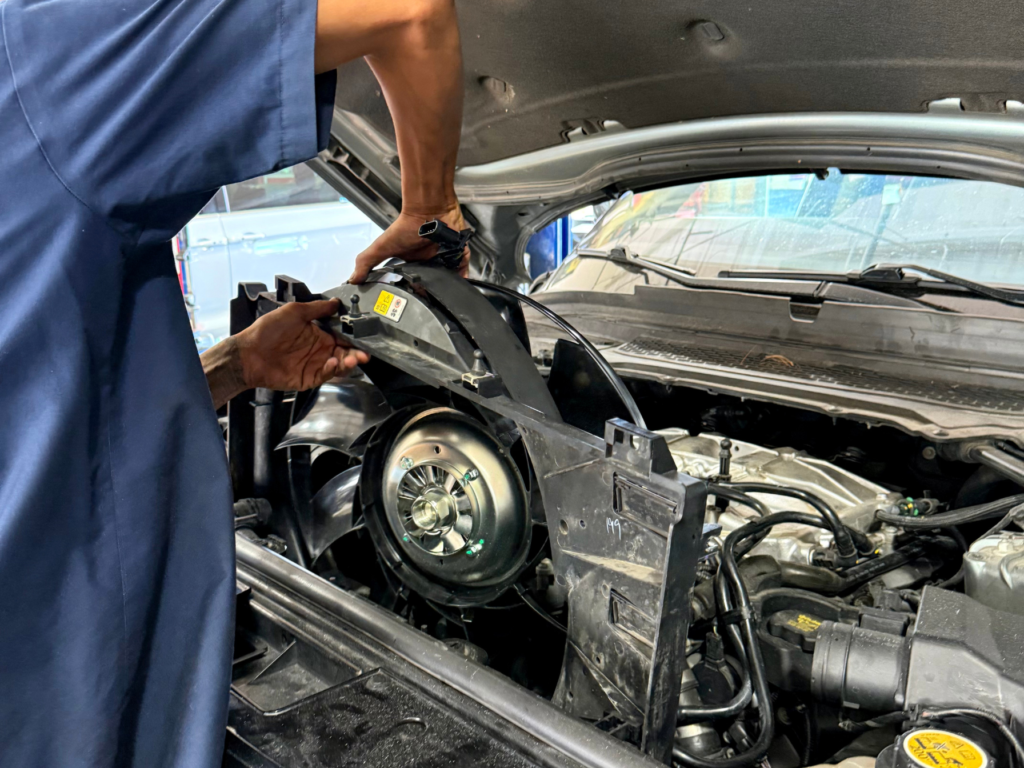 Technician holding a cooling fan and shroud assembly beside an open engine bay