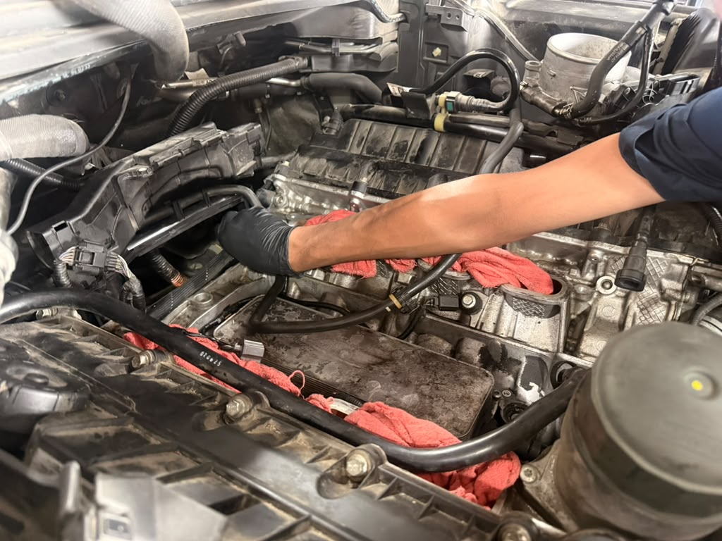 Gloved technician working among hoses and exposed components in an engine bay