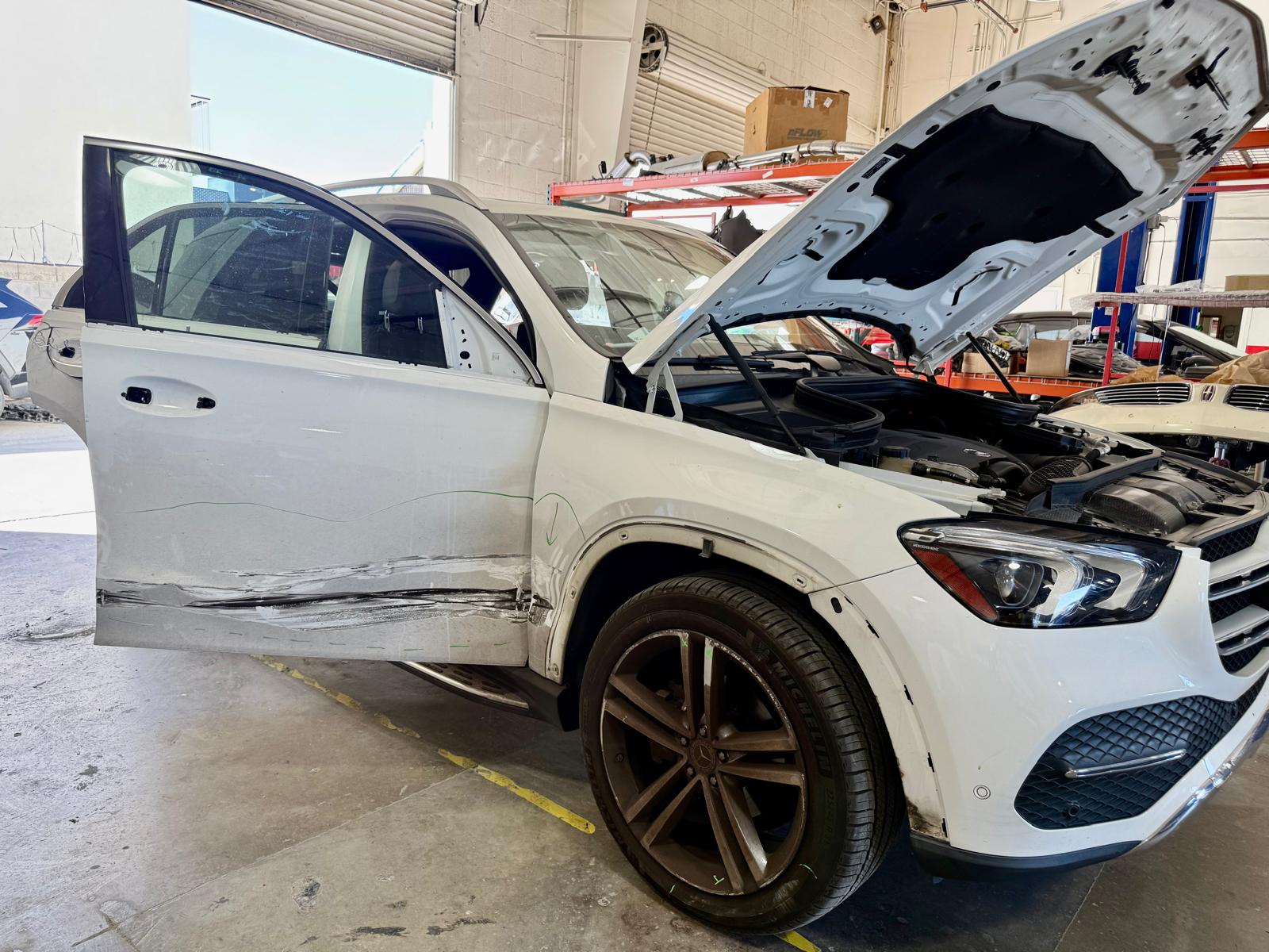 White Mercedes-Benz SUV with visible side collision damage, removed trim and open hood inside Universal Motorcars