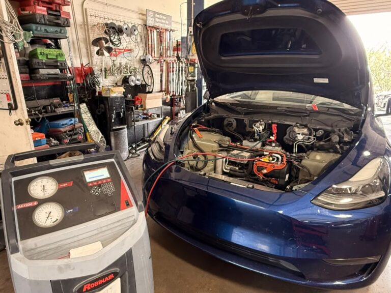 Blue Tesla with its hood open and A/C service equipment connected in the Universal Motorcars workshop