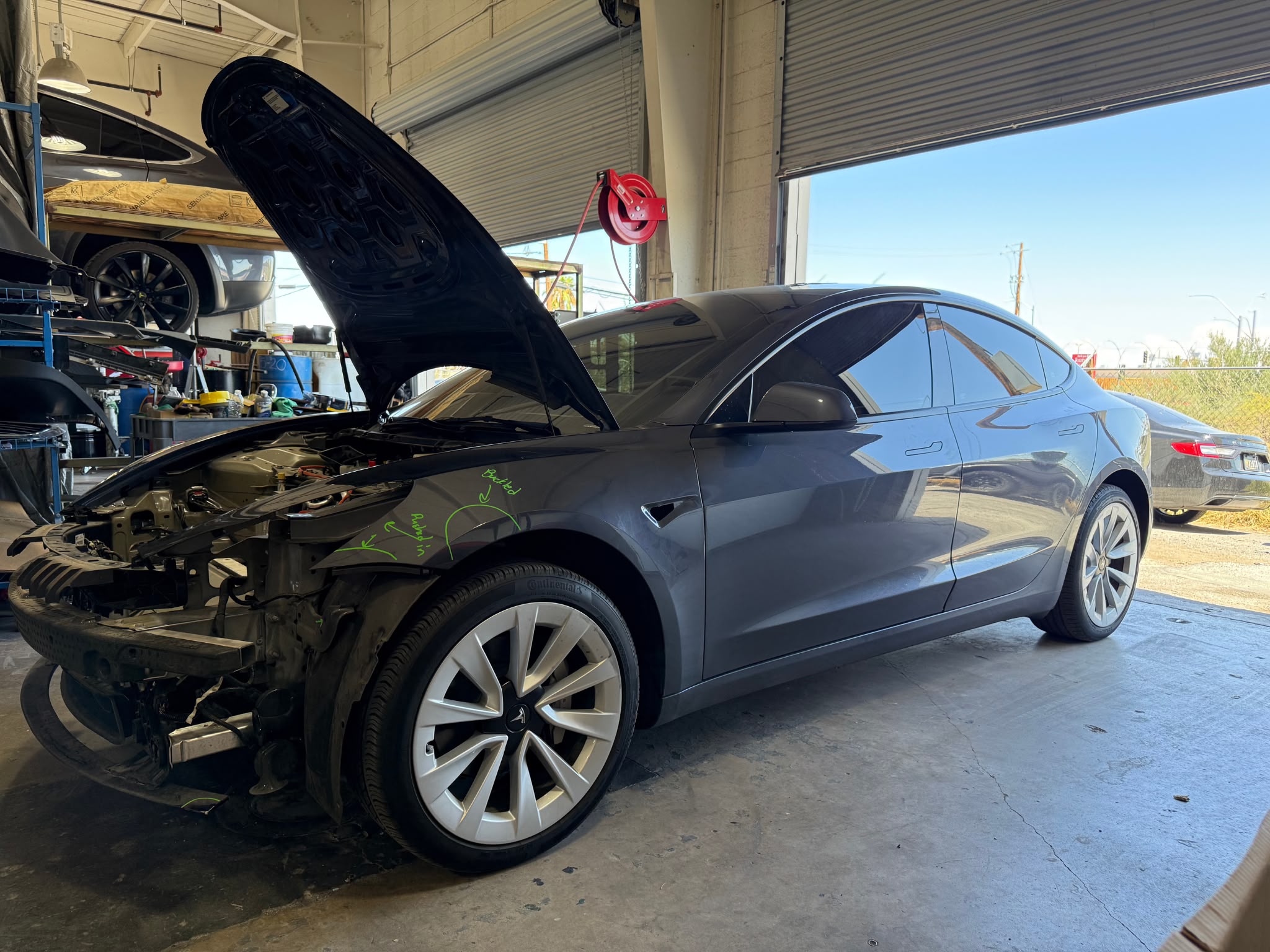 Tesla Model 3 in the Universal Motorcars repair bay with its front bumper removed and damage marked on the fender