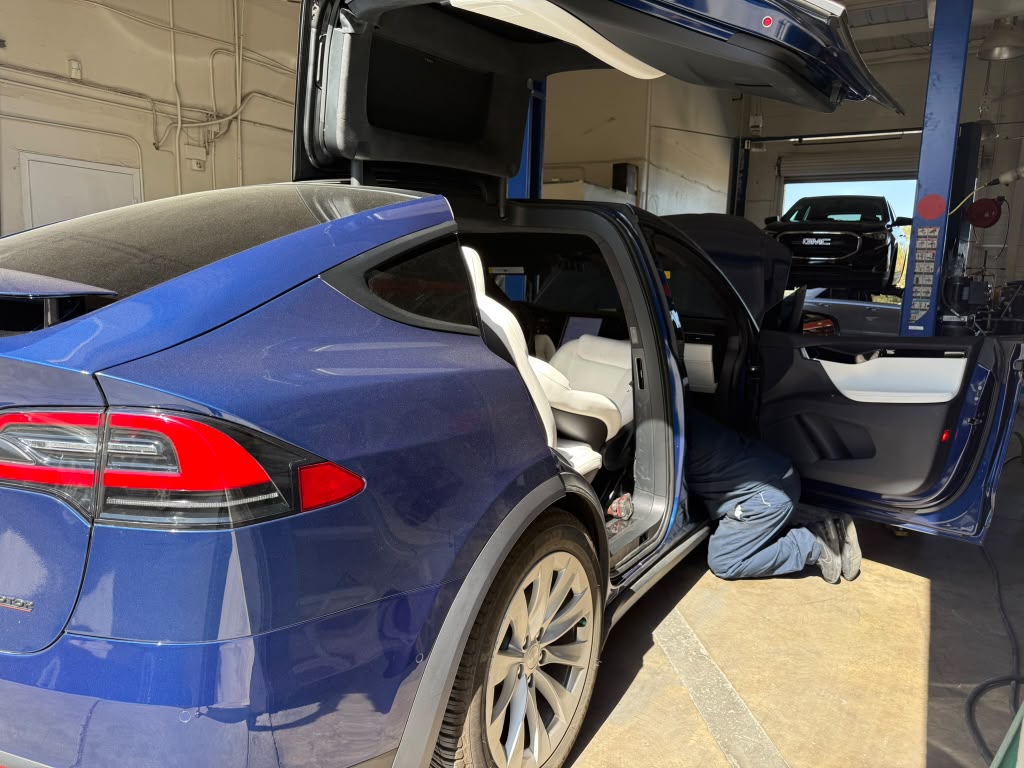 Technician beside a blue Tesla Model X with its falcon-wing door open at Universal Motorcars