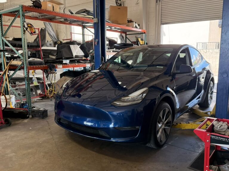 Blue Tesla Model Y positioned between the lifts in the Universal Motorcars service bay