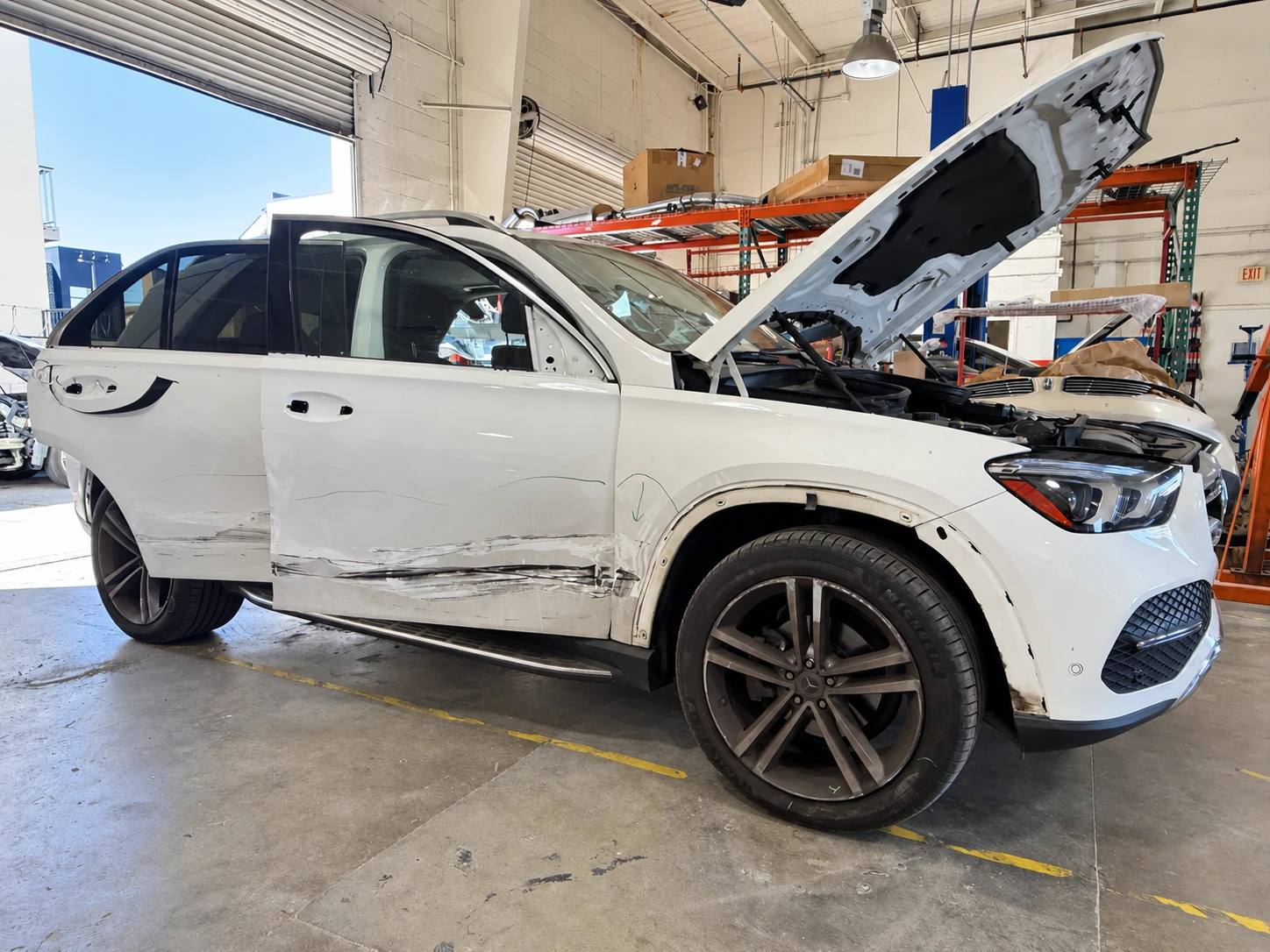 White Mercedes-Benz SUV with scraping and collision damage along the passenger-side doors before repair