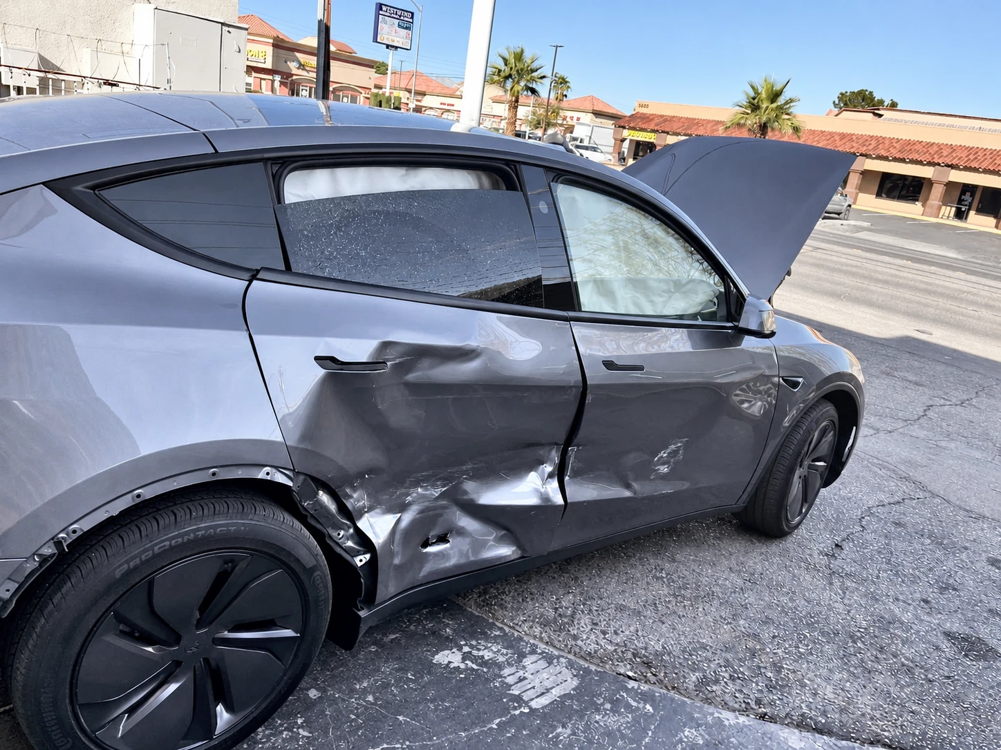 Gray Tesla with crushed passenger-side doors and missing wheel-arch trim before collision repair