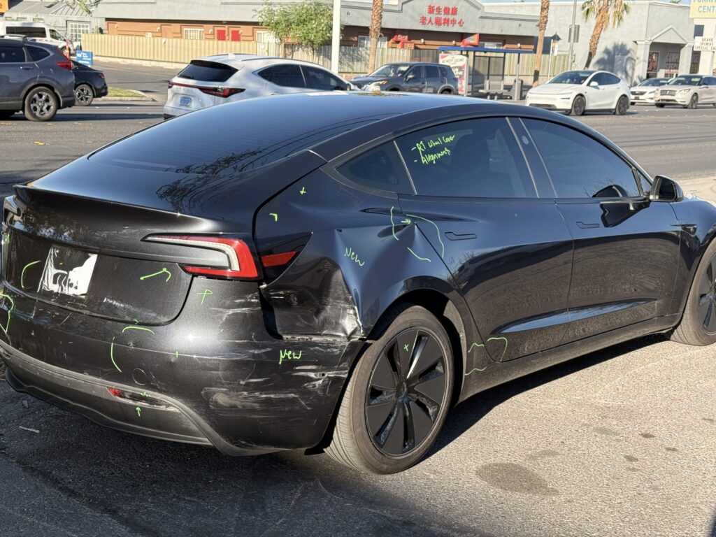 Dark Tesla sedan with bumper-cover scrapes and a dented rear quarter panel