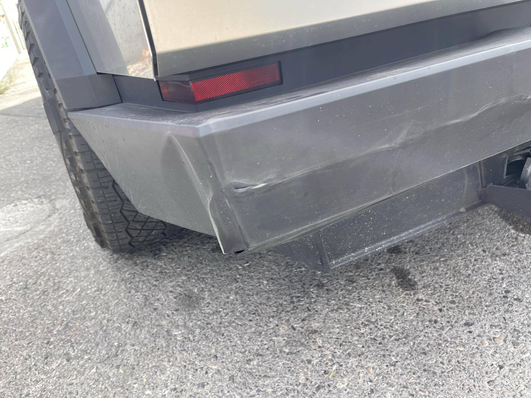Close-up of creasing, scraping and a split near the left corner of the Cybertruck rear bumper