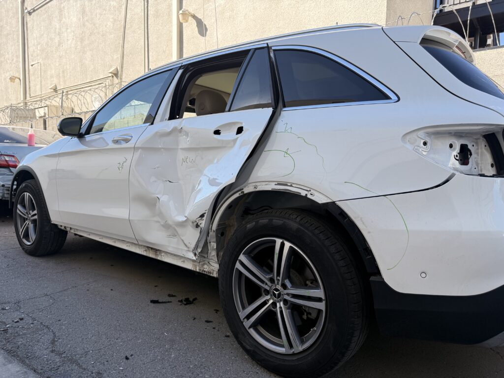 White Mercedes-Benz SUV with a deeply dented rear door and damage around the rear wheel opening