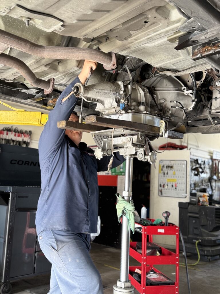 Technician working beside a transmission supported beneath a raised vehicle