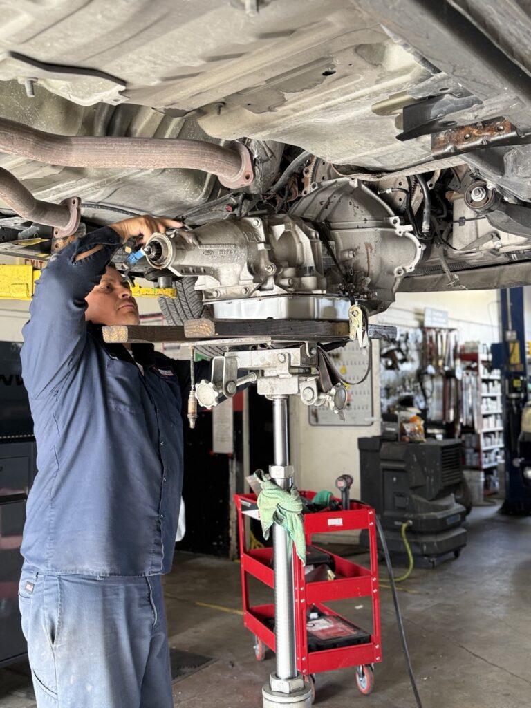 Technician positioning a transmission beneath a vehicle on a lift