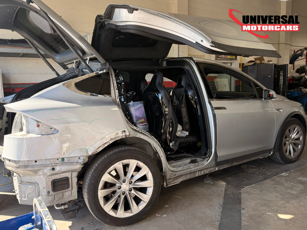 Silver Tesla Model X with rear quarter-panel damage exposed for repair at Universal Motorcars