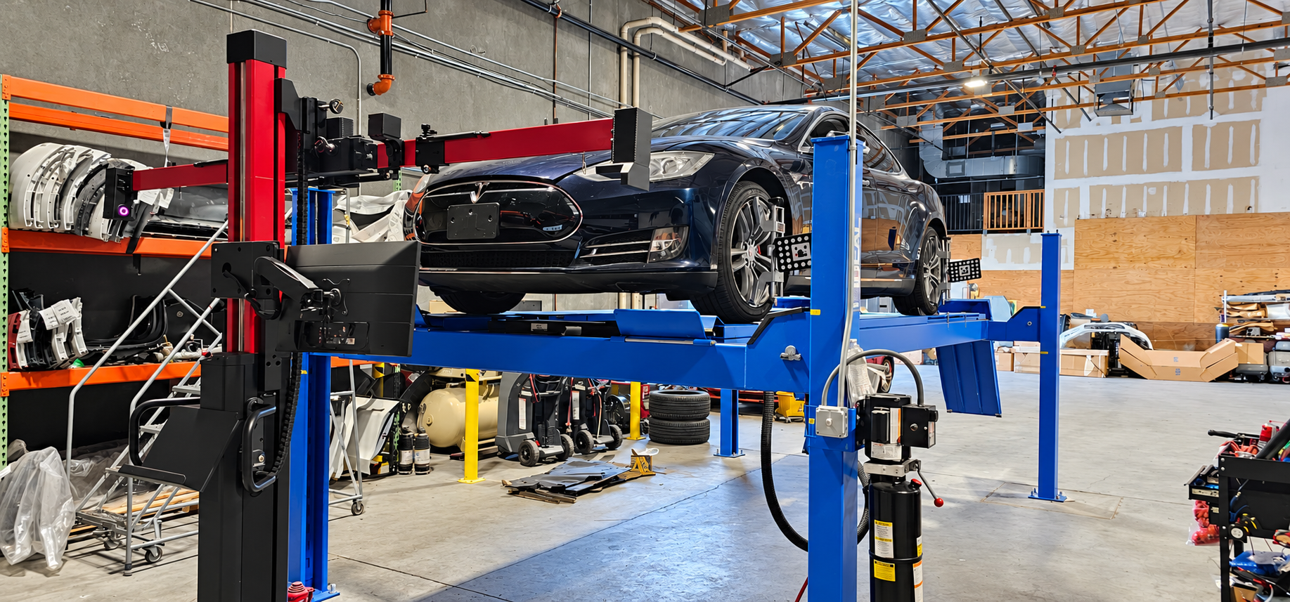 Dark blue Tesla on an alignment rack with wheel-mounted alignment targets