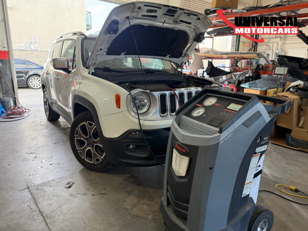 Jeep with its hood open beside A/C service equipment in the Universal Motorcars workshop.