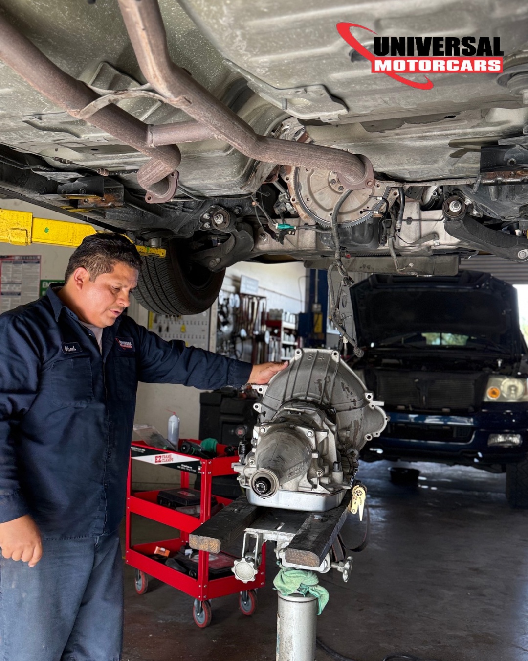 Universal Motorcars technician beside a removed transmission on a support stand