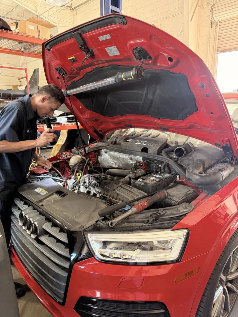 Universal Motorcars technician working under the open hood of a red Audi