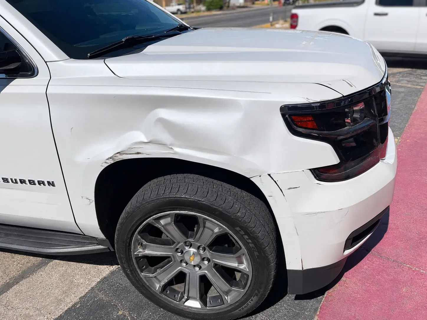 Dent and paint damage on the front fender of a white Chevrolet Suburban.