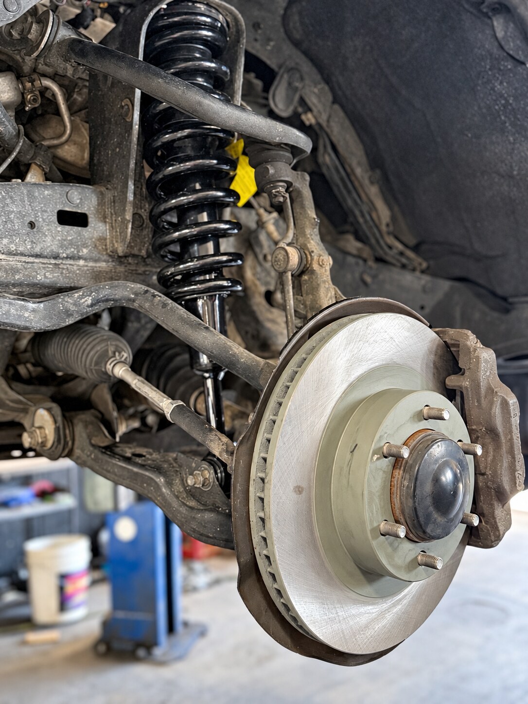 Coil spring, shock absorber and control arms behind an exposed brake rotor.