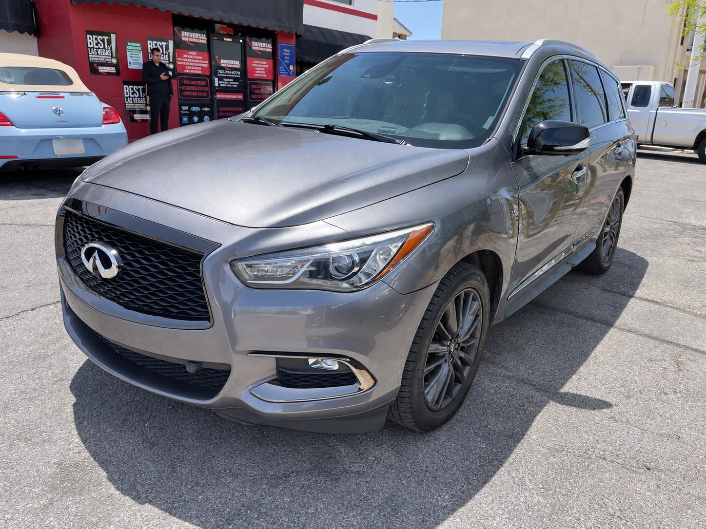 Gray INFINITI SUV outside the Universal Motorcars body shop, viewed from the front driver side.