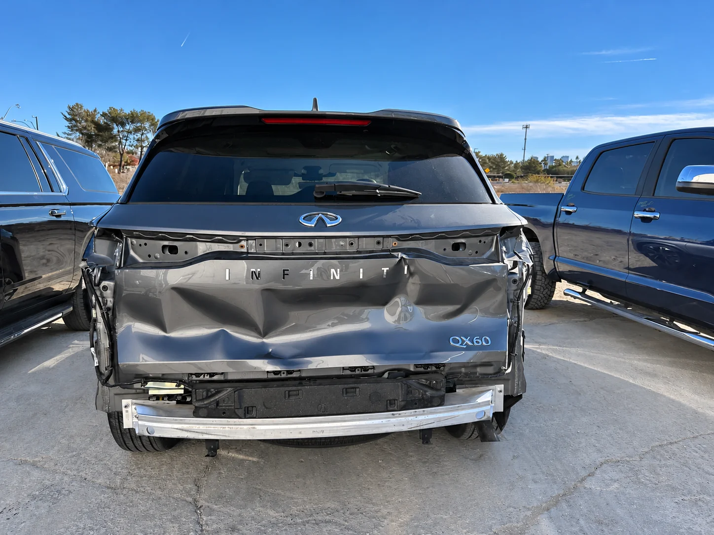 Rear collision damage on an INFINITI QX60, with a crushed liftgate and the rear bumper cover removed.