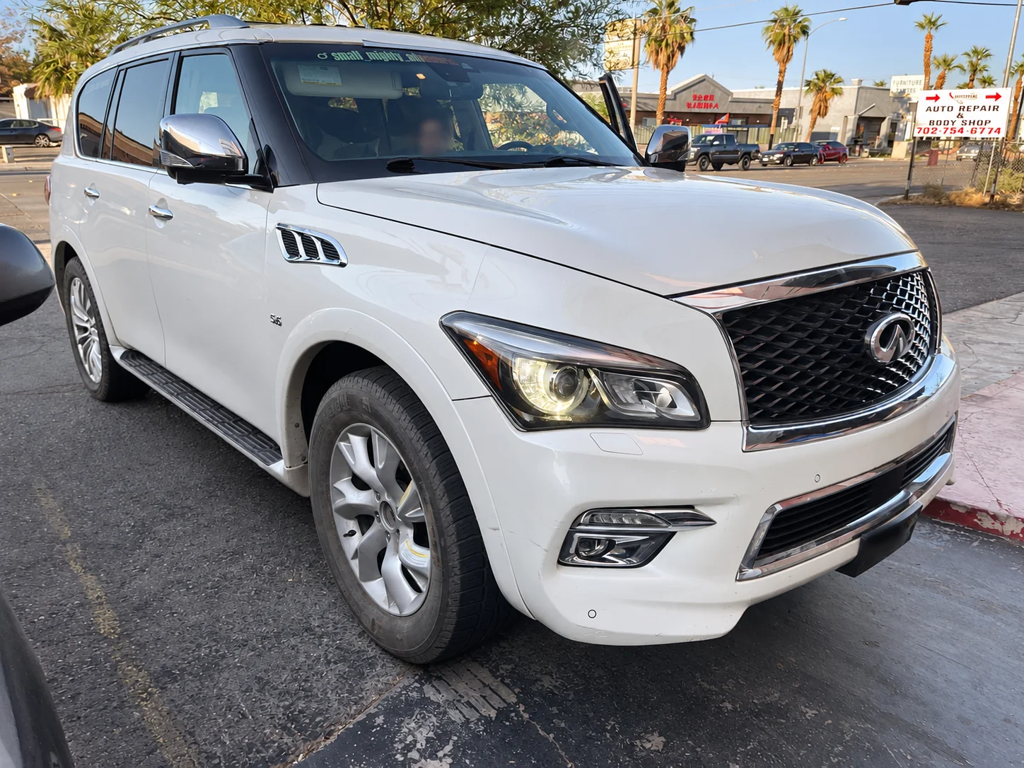 White INFINITI SUV outside Universal Motorcars in Las Vegas, showing the front bumper, fender and passenger side.