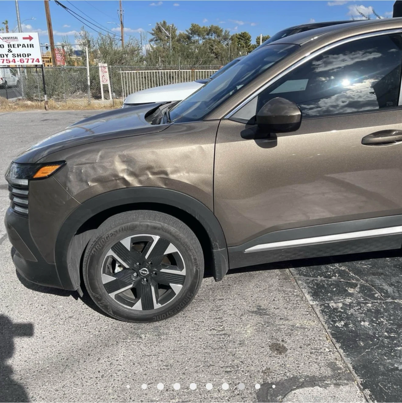 Bronze Nissan with a dented front fender and driver’s door outside Universal Motorcars in Las Vegas.