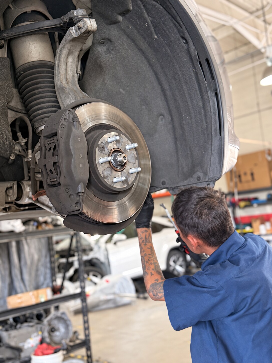 Technician beside exposed brake and suspension components with the vehicle wheel removed.