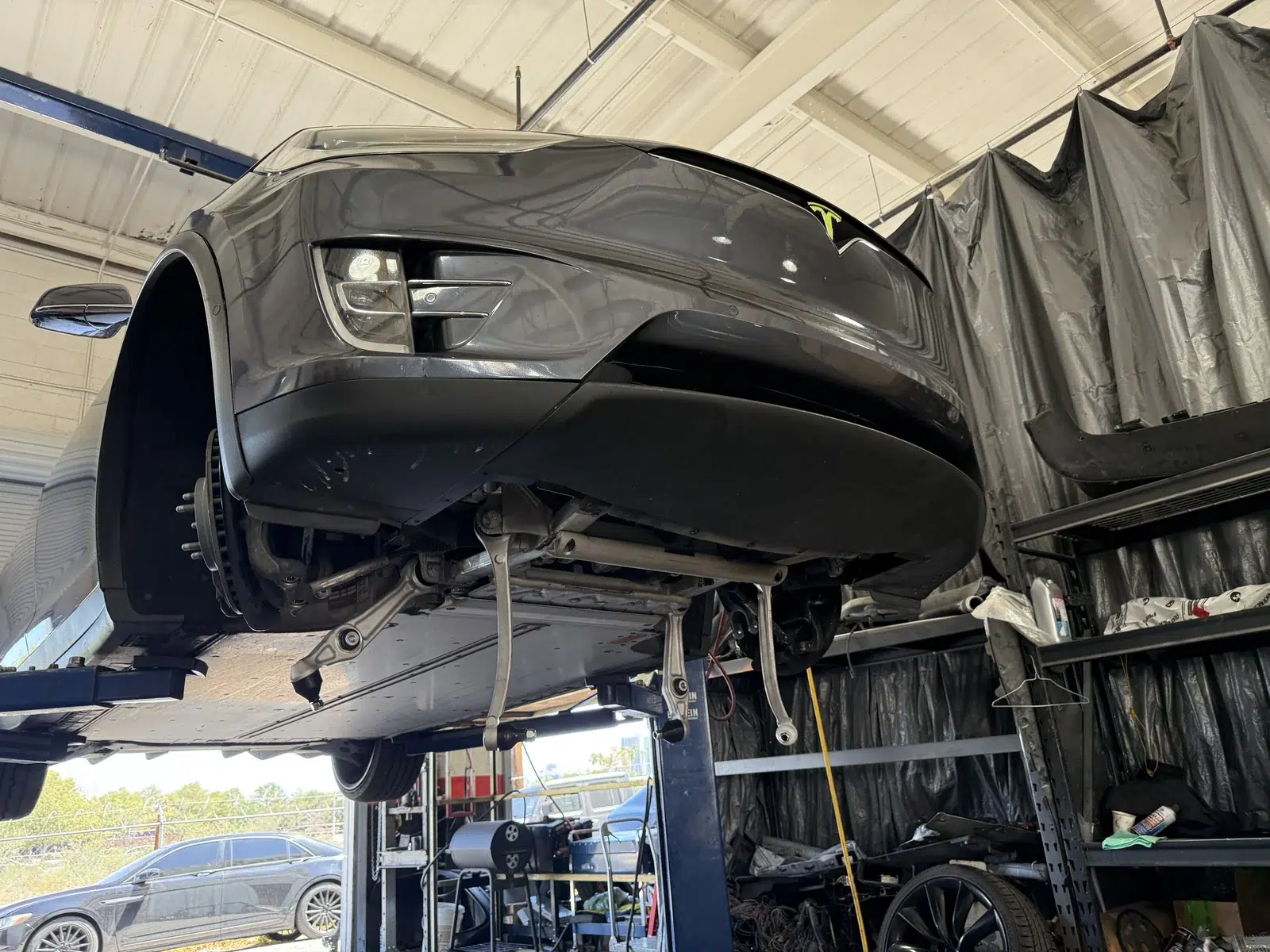 Tesla raised on a workshop lift with front wheels removed and suspension components exposed at Universal Motorcars