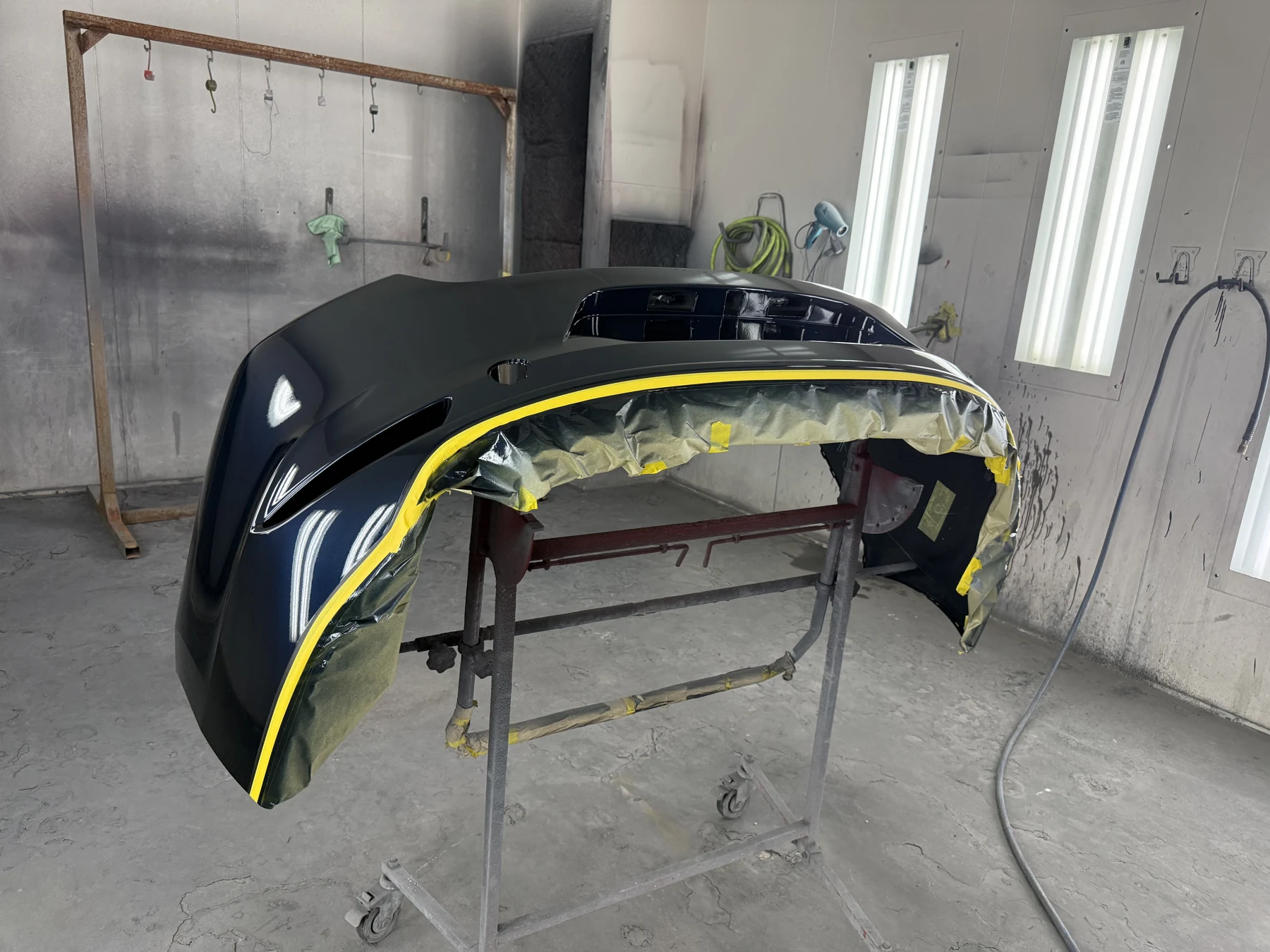 Glossy dark blue bumper on a stand in Universal Motorcars’ paint area