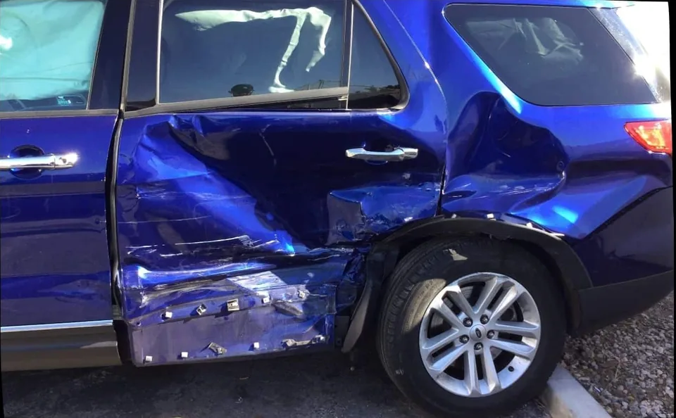 Blue Ford Explorer with visible damage along its side doors before repair