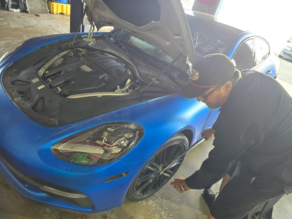 Technician working along the front fender of a blue Porsche Panamera