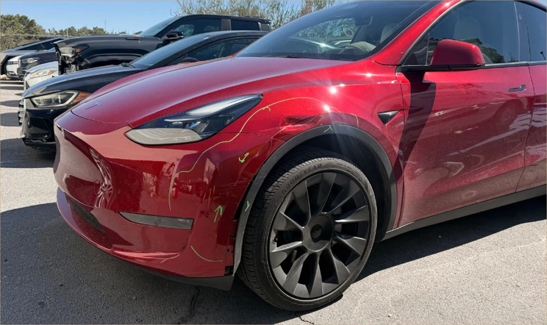 Red Tesla Model Y before repair, with damage at the left front fender and bumper
