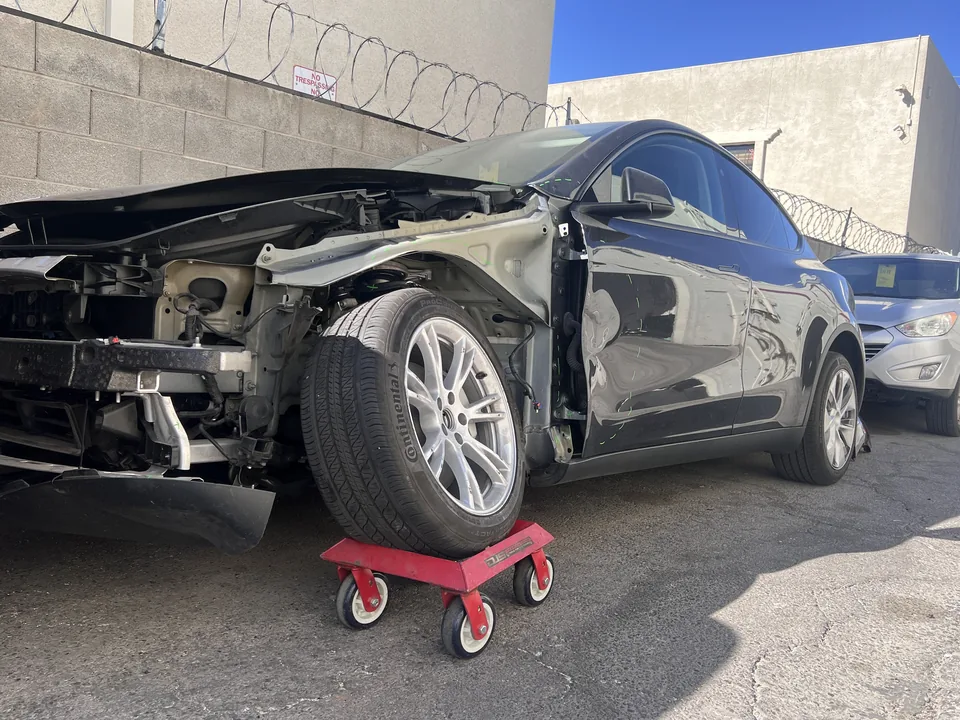 Dark Tesla Model Y with front bodywork removed during collision repair