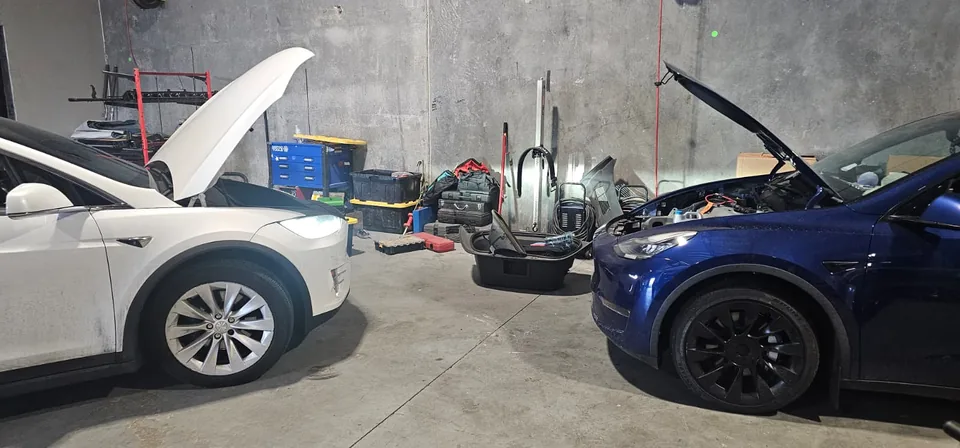 White and blue Tesla Model Y vehicles with their hoods open in the workshop