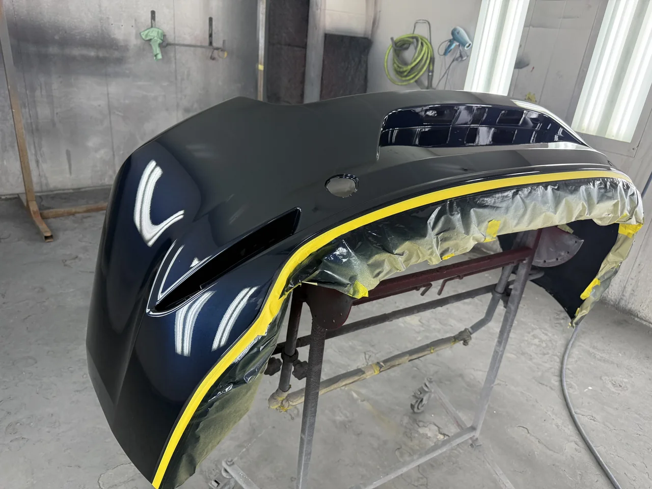 Dark blue bumper with a glossy finish on a stand inside the Universal Motorcars paint booth.