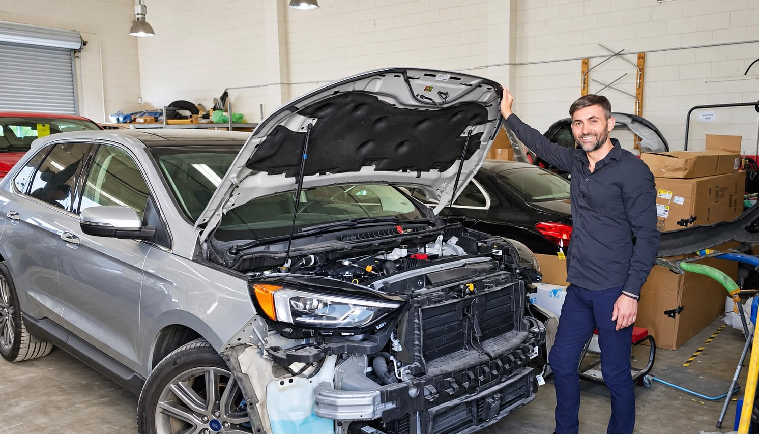 Universal Motorcars team member beside a silver Ford SUV with the hood open and front bumper removed.