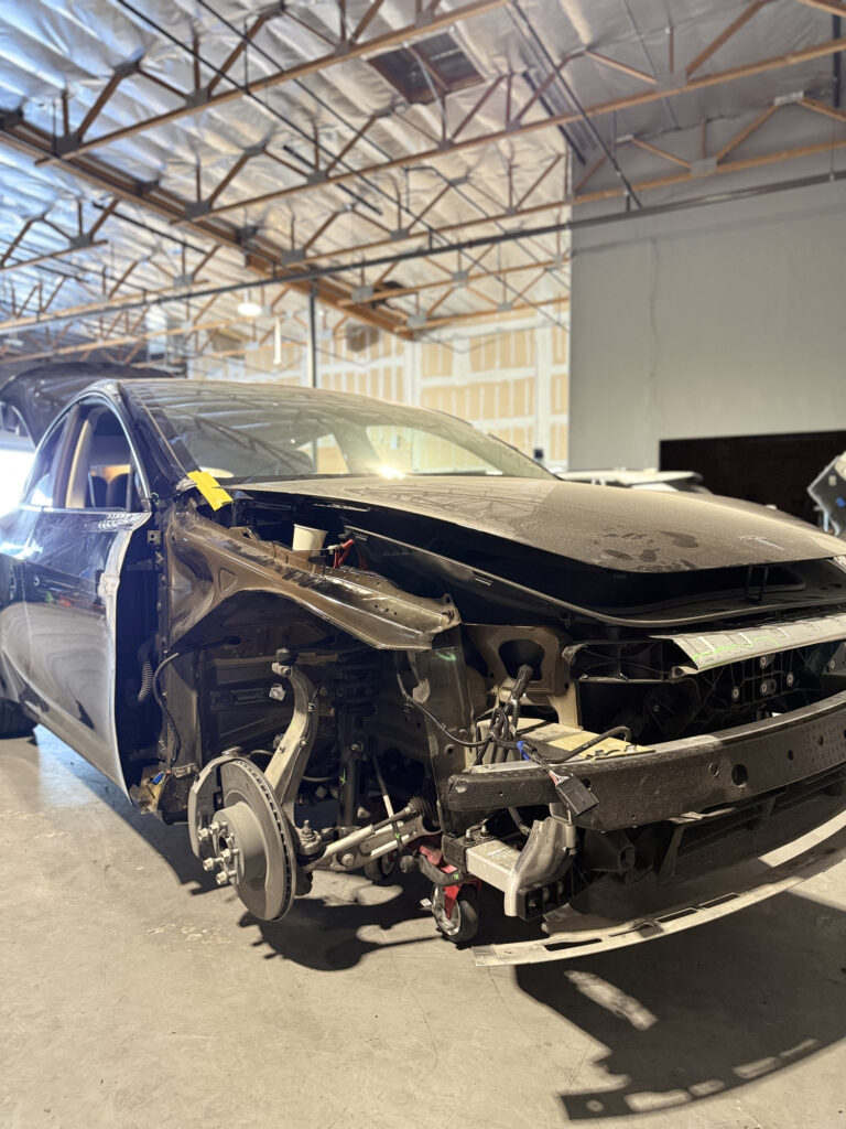 Vehicle with front body panels removed, exposing its front structure inside the collision workshop.