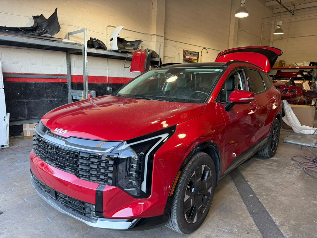 Red Kia SUV inside Universal Motorcars’ body shop, with its rear liftgate open.