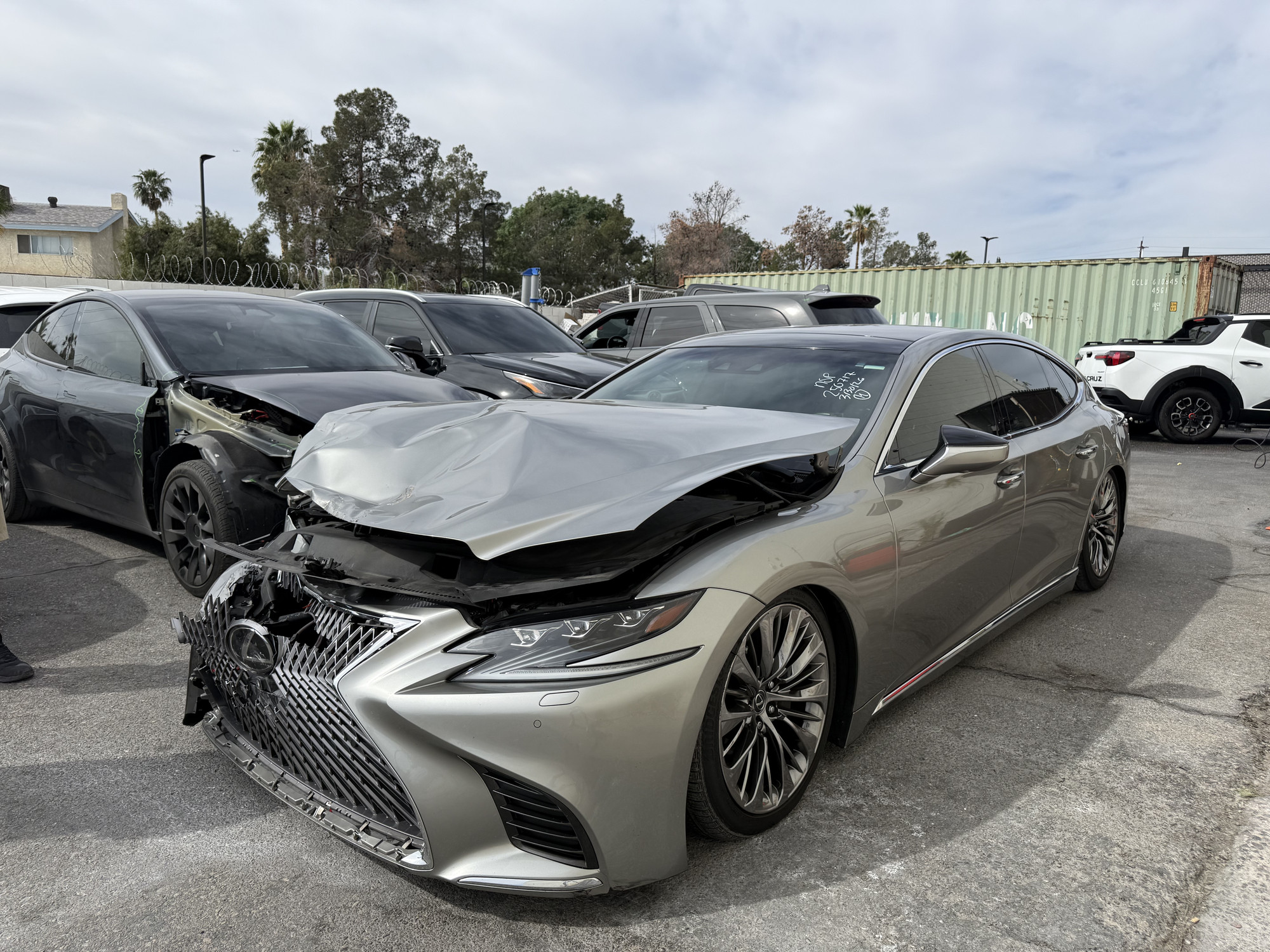 Silver Lexus sedan with visible front-end and hood damage in the repair yard.