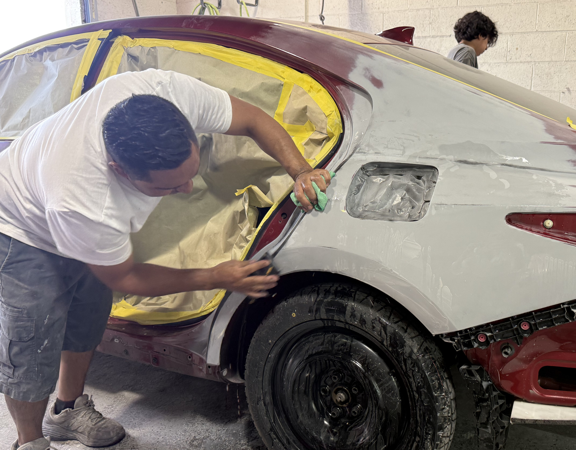 Technician preparing a masked vehicle rear-quarter panel in the body shop.