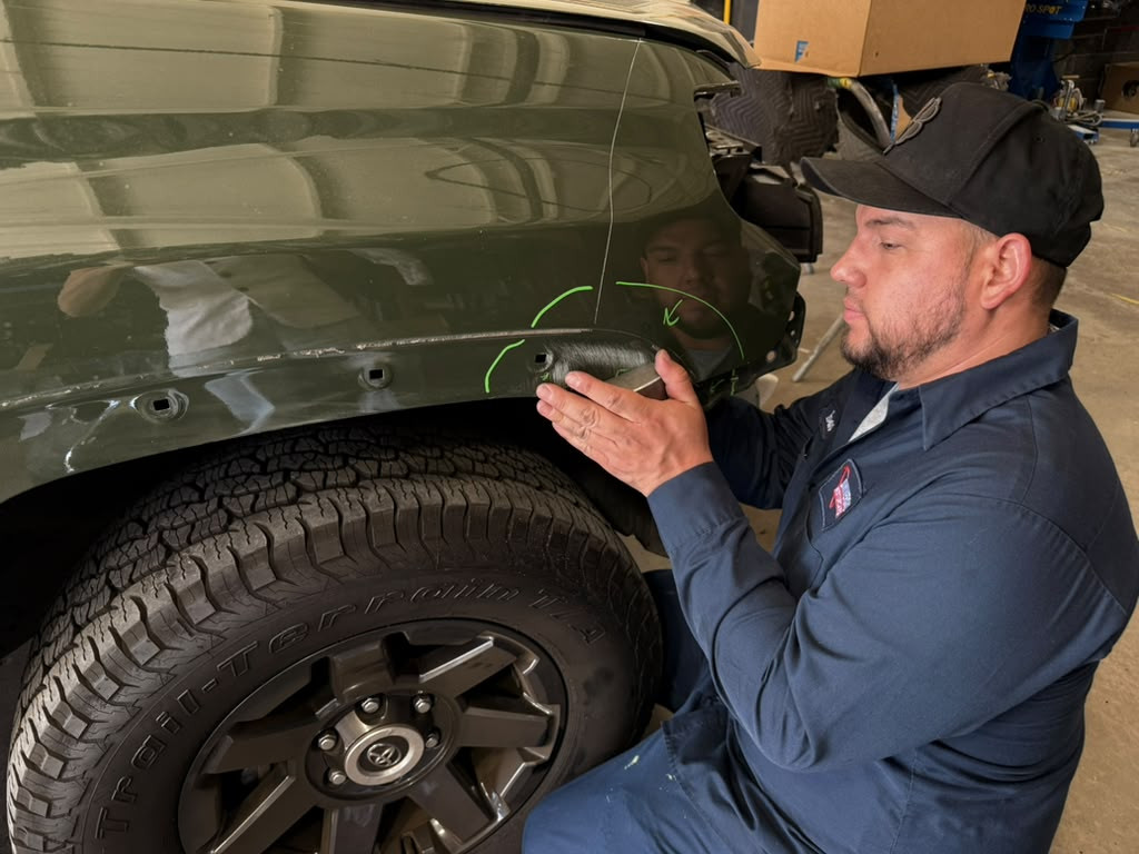 Technician examining a marked rear-quarter body panel on a Toyota in the workshop.
