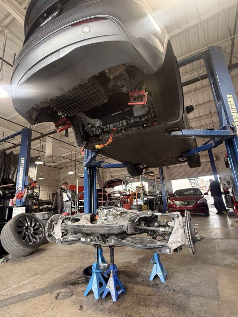 Angled view of Tesla mechanical work at Universal Motorcars, showing the vehicle above the removed rear assembly.