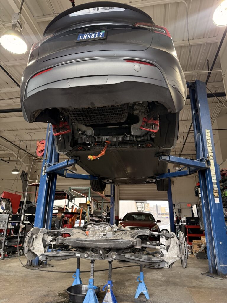 Tesla raised on a lift at Universal Motorcars with its rear subframe and drive assembly removed.
