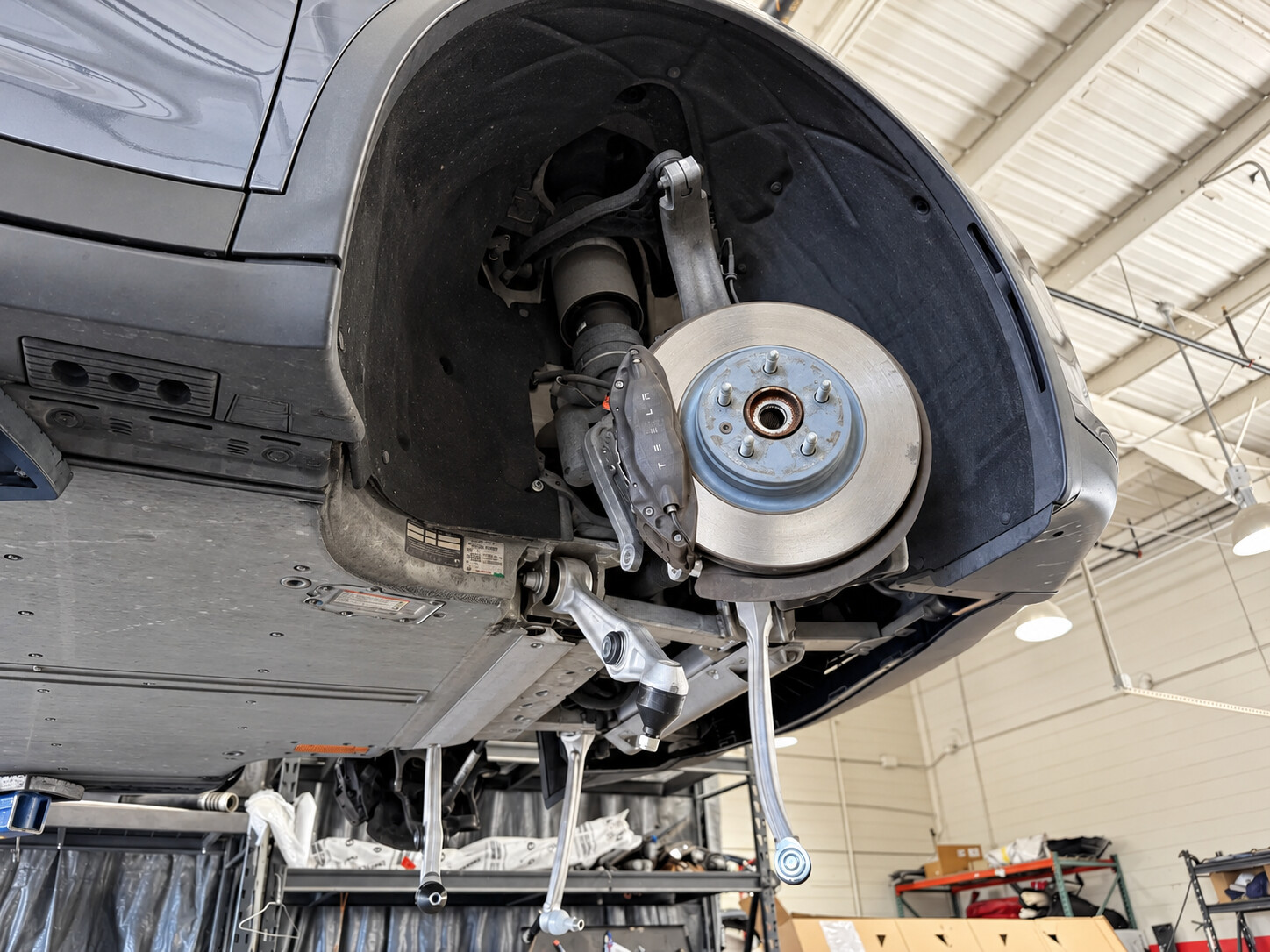 Exposed Tesla brake rotor and suspension components with the wheel removed in a workshop.