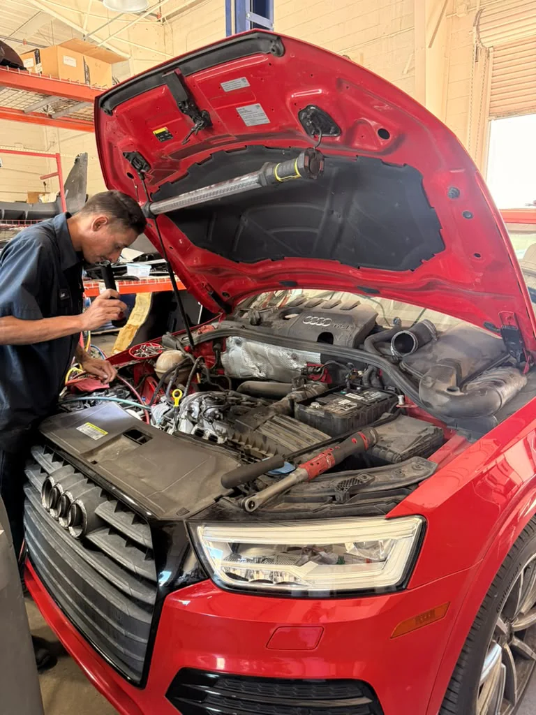 Technician working in the engine bay of a red Audi with its hood open
